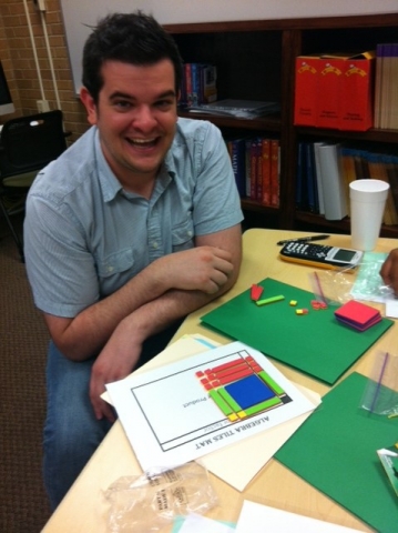 A single studnet at a talbe that is covered in craft supplies and he is smiling at the camera.