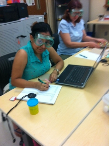 Student wearing safety goggles looking up from her laptop.